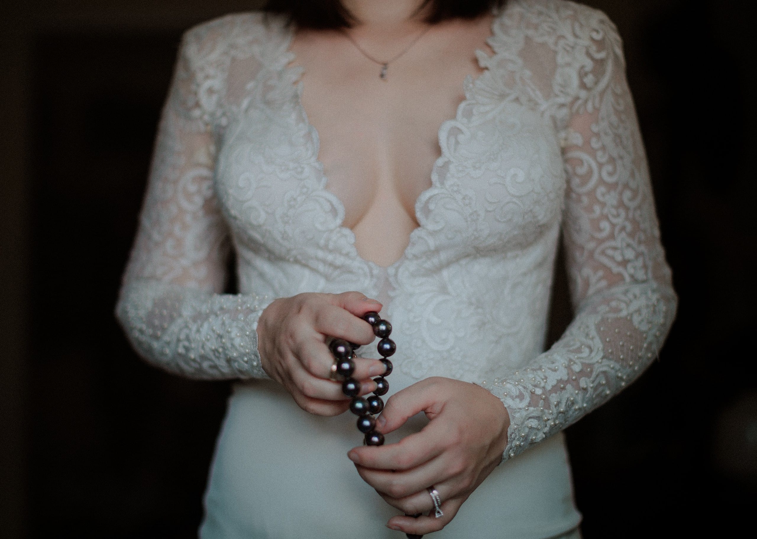 Bride in wedding dress holds black pearls