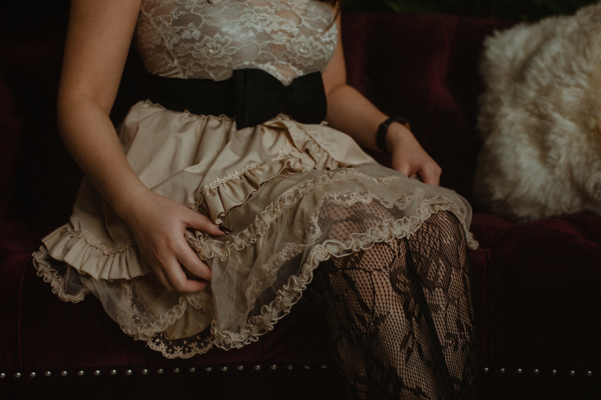 Girl sits on red velvet couch fluffing white lace dress