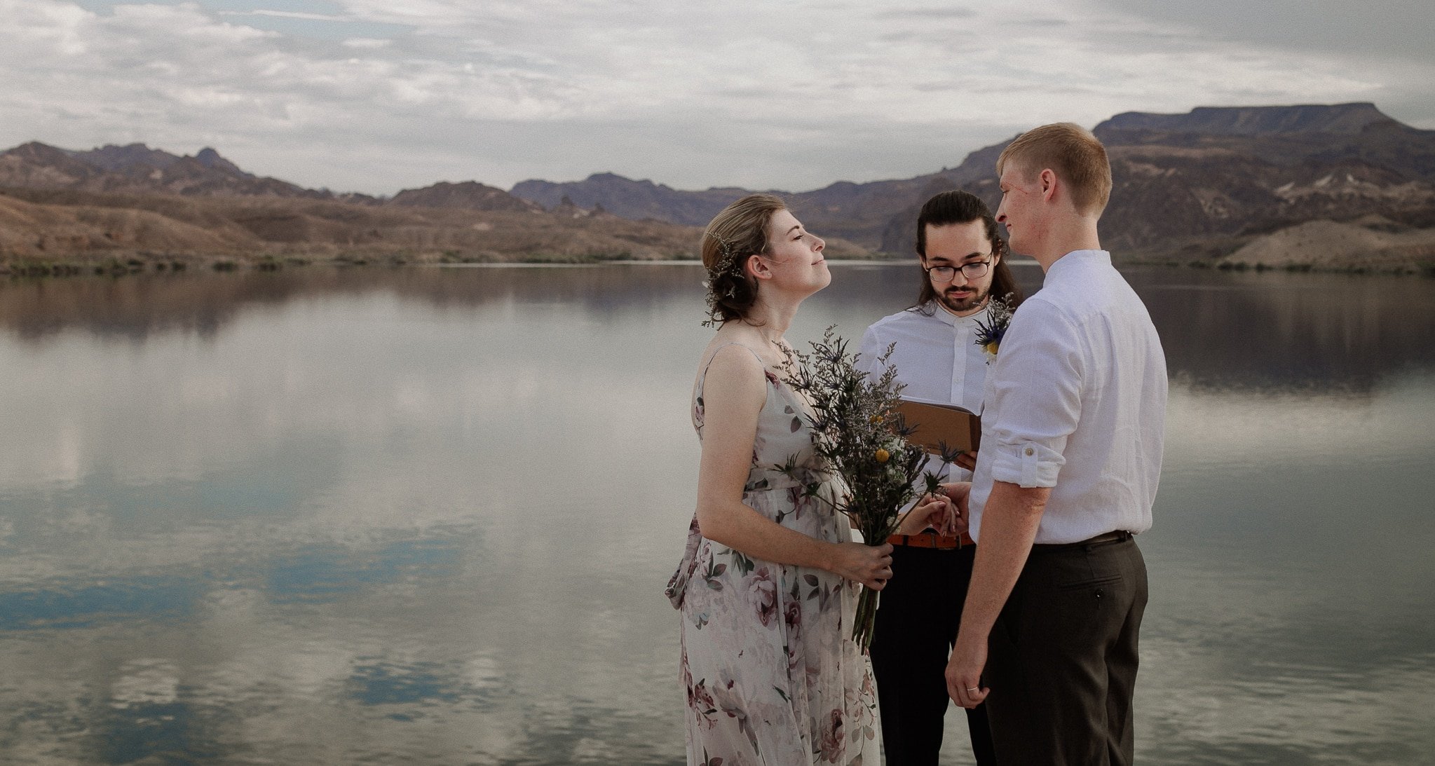 Bride and groom stand at edge of cliff over Colorado River at sunrise
