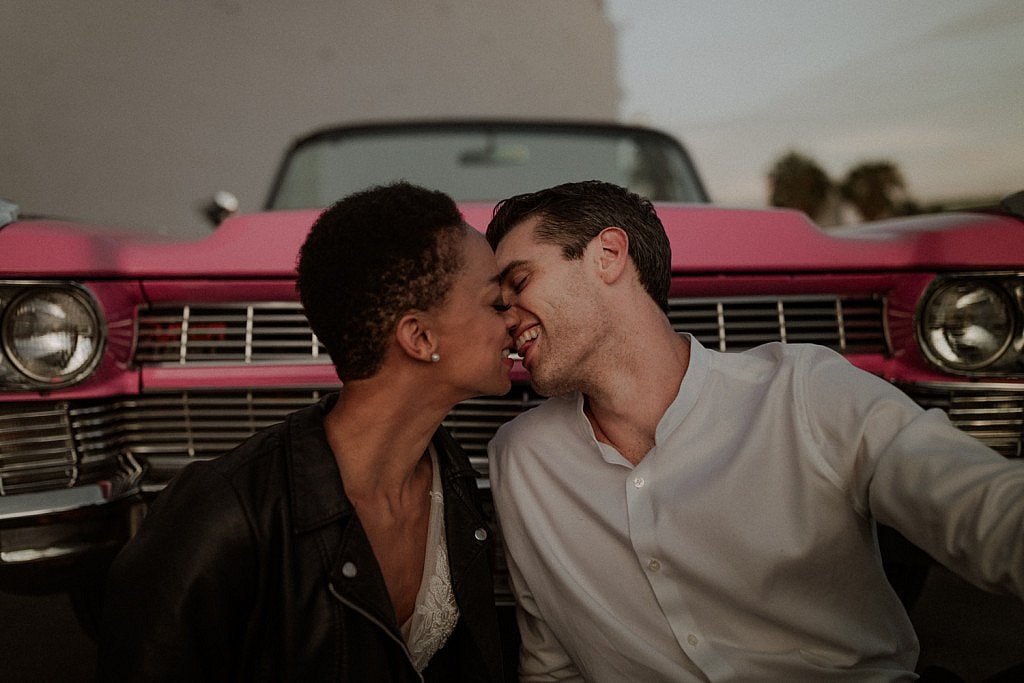 Mixed race wedding couple in downtown Vegas sit in front of Pink Caddy car with leather jacket