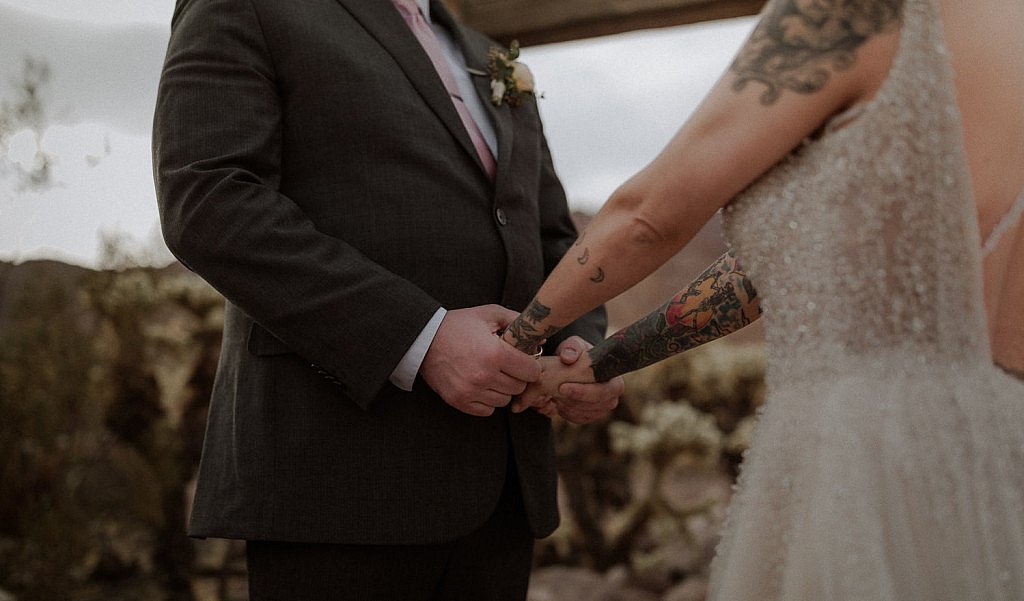 Couple holds hands during ceremony at sunset