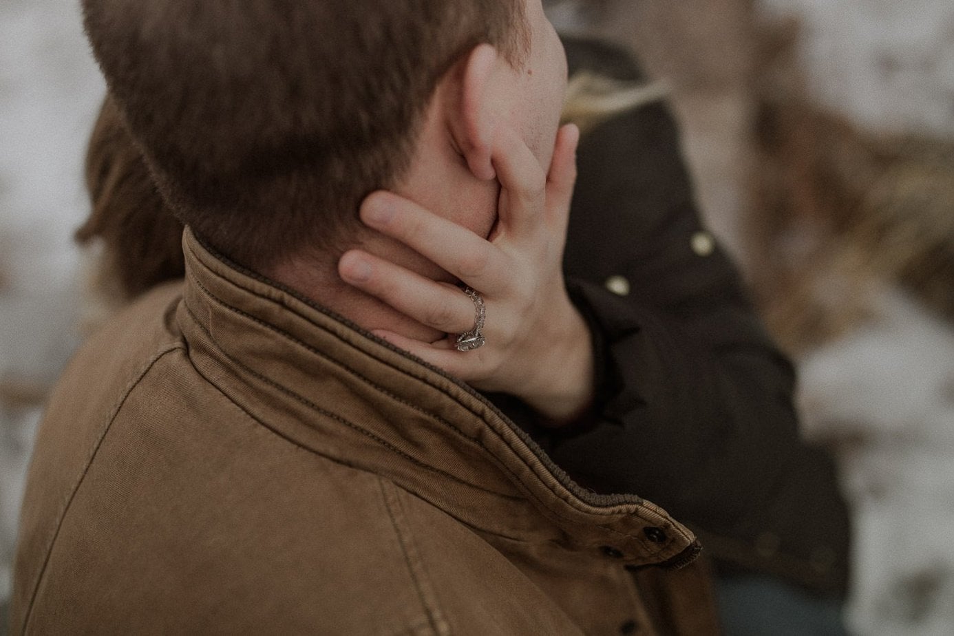 Close up image of the engagement ring during an adventure engagement session in the mountains. The snow is slowly melting around the couple but they still have their coats on. Niki holds her fiance's face