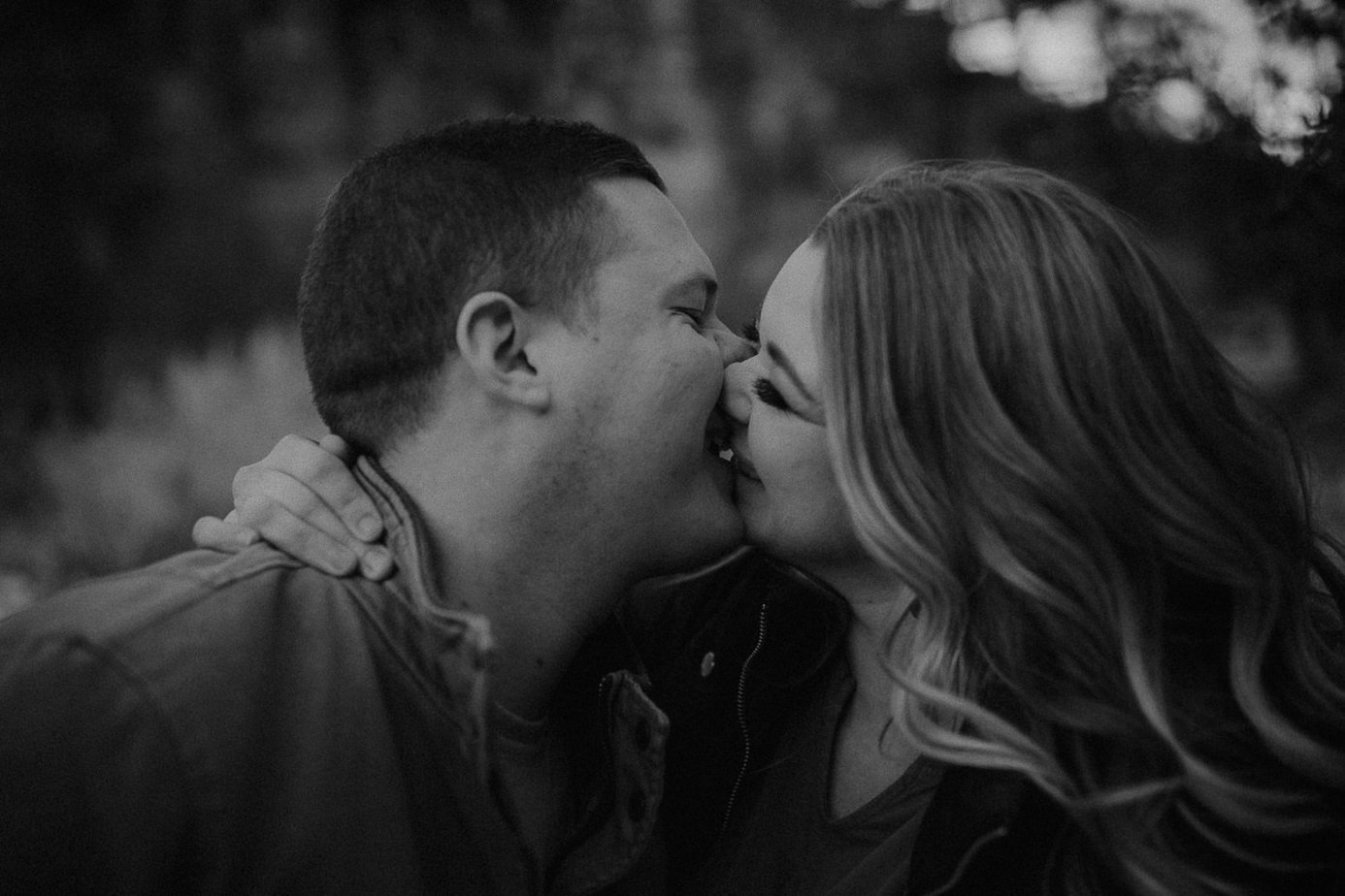 Couple laughs and kisses each other in this black and white image.