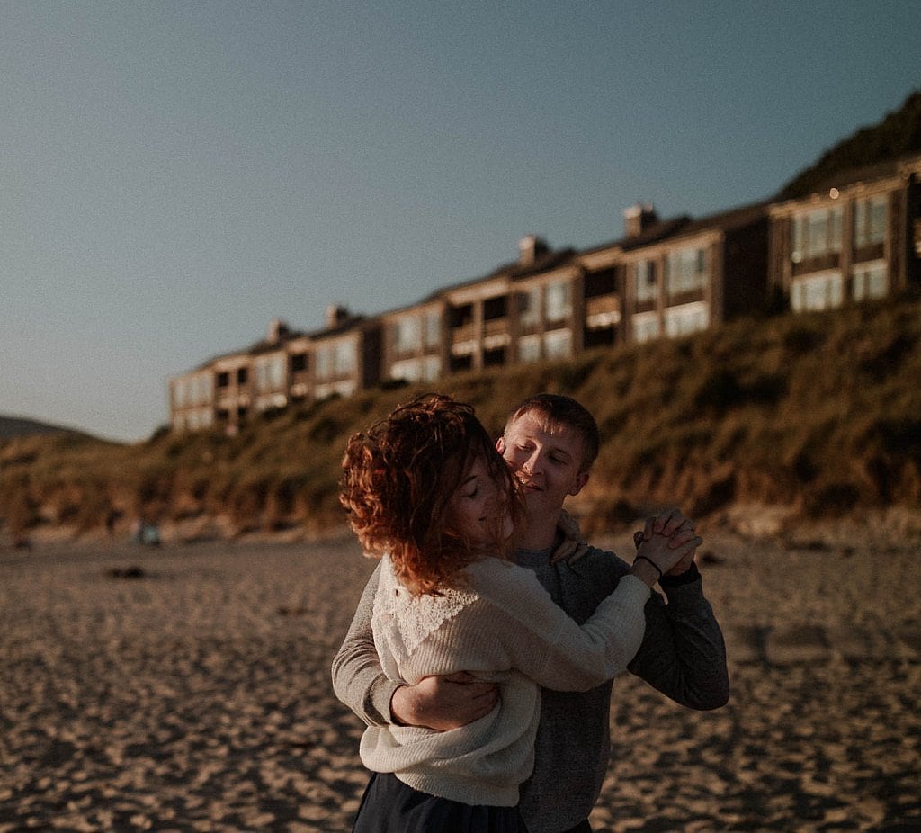 Groom wraps his arms around his bride for their first dance at their elopement on the beach. The Oregon coast wind blows her red hair around her face as the bride holds onto him