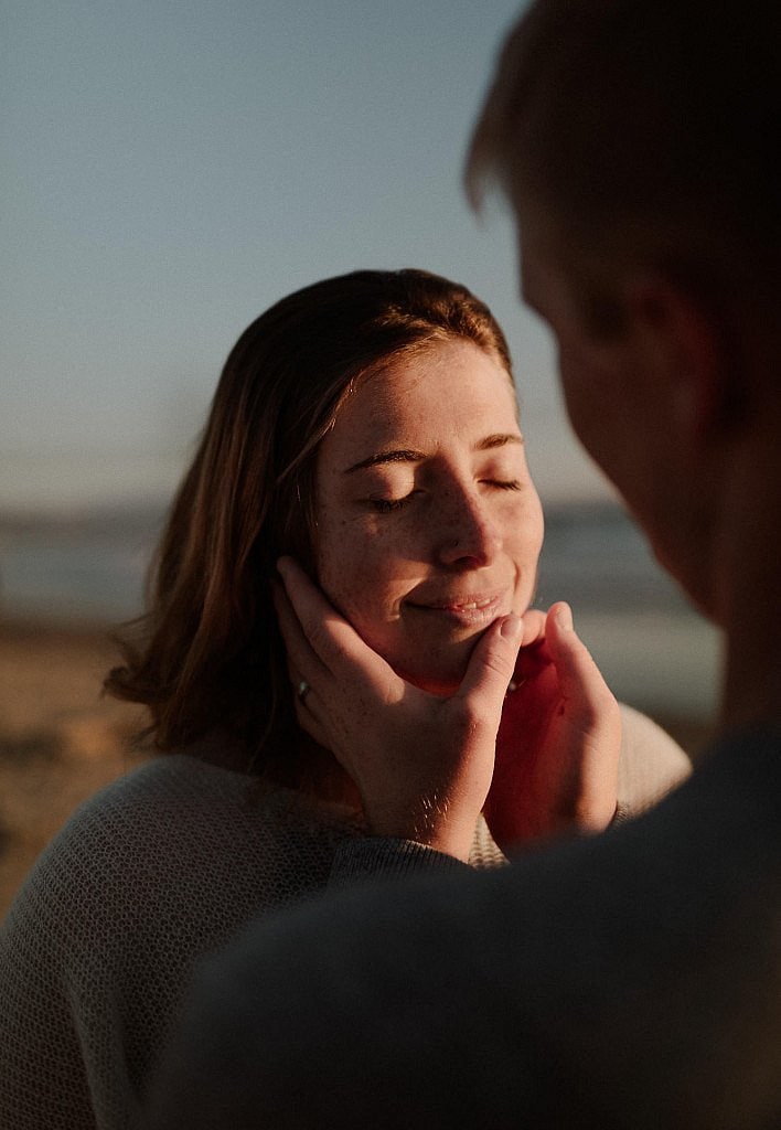 Groom touches brides face during their romantic elopement ceremony. Sunset elopement on the beach at Cape Kiwanda on the Oregon coast was so romantic