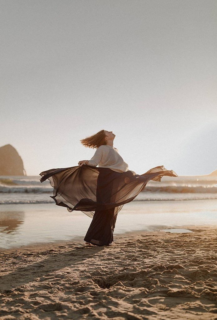 Carefree bride dances in the light of the setting sun after her elopement ceremony on the Oregon Coast at Cape Kiwanda