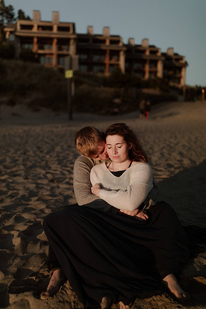 Bride and groom snuggle in the sand after their Pacific City Beach Elopement at sunset