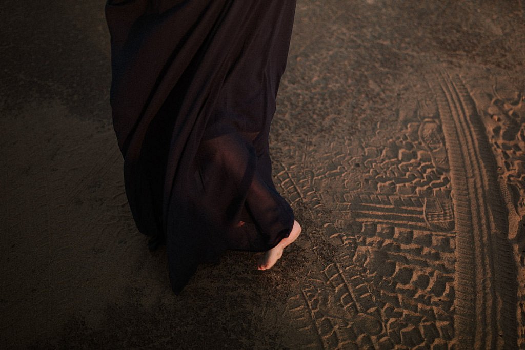 Bride walks barefoot in the sand. Her flowy blue elopement dress wraps around her ankles in the wind