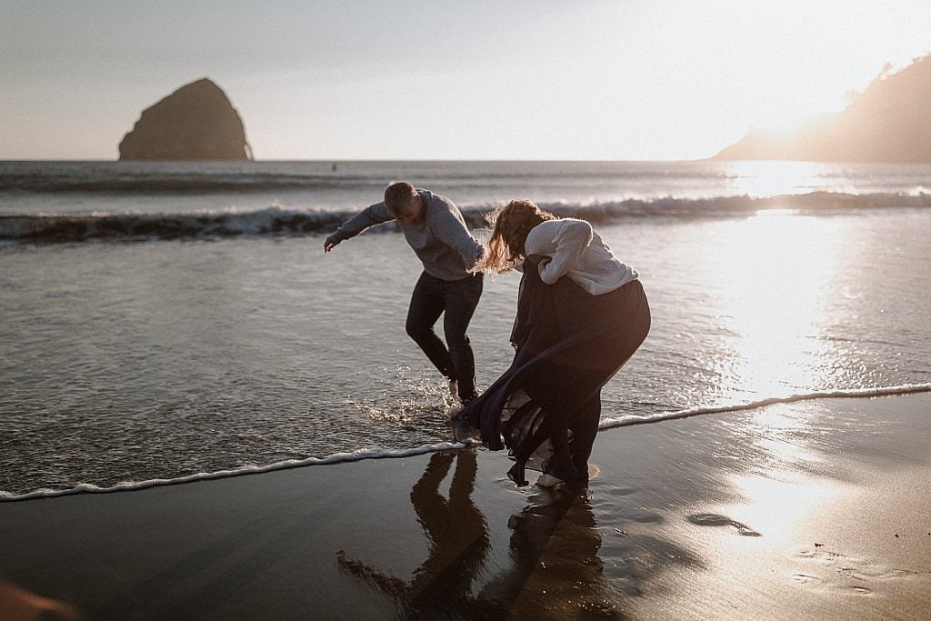Groom tries to pull bride into the cold water on the Oregon Coast at Cape Kiwanda but she tries to stay dry