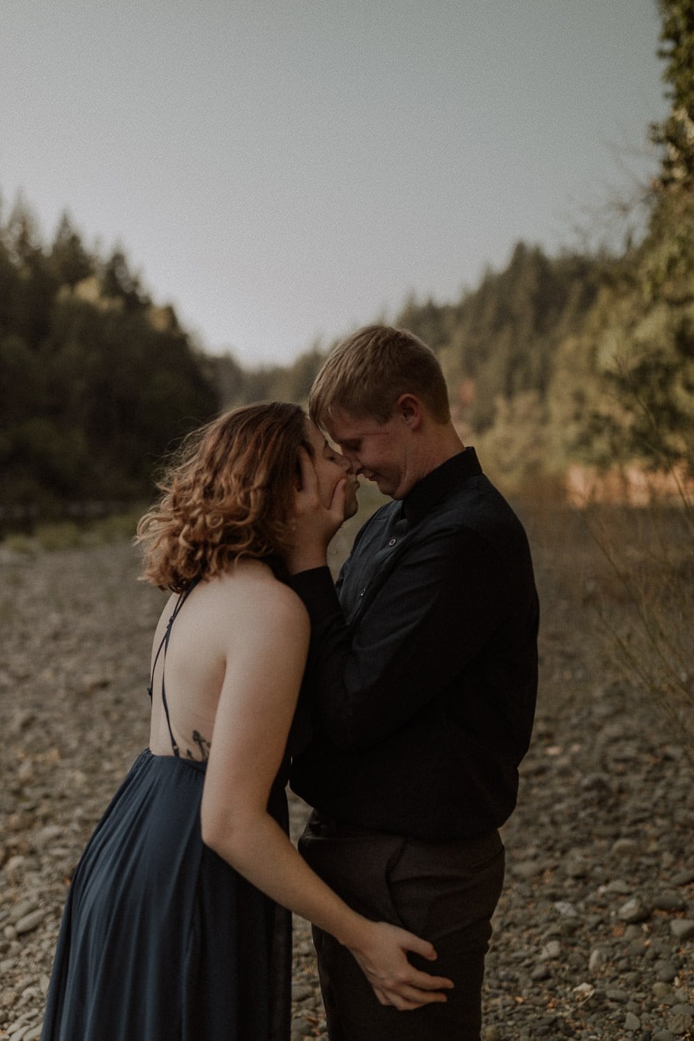 Moody elopement in the red woods forest in Northern California. Bride wears a navy blue elopement dress and is snuggling close to her partner by the river