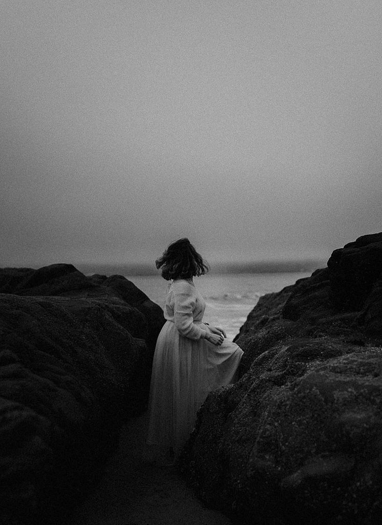 Foggy morning at Baker Beach bridal session. Adventurous bride climbs over the rocks on the beach while the sun rises