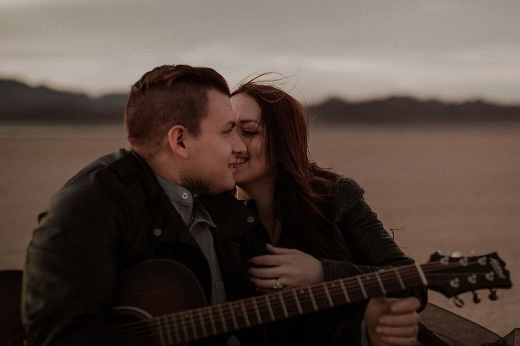 Dry lake bed elopement in Las Vegas at sunset groom play guitar for bride while drinking beer
