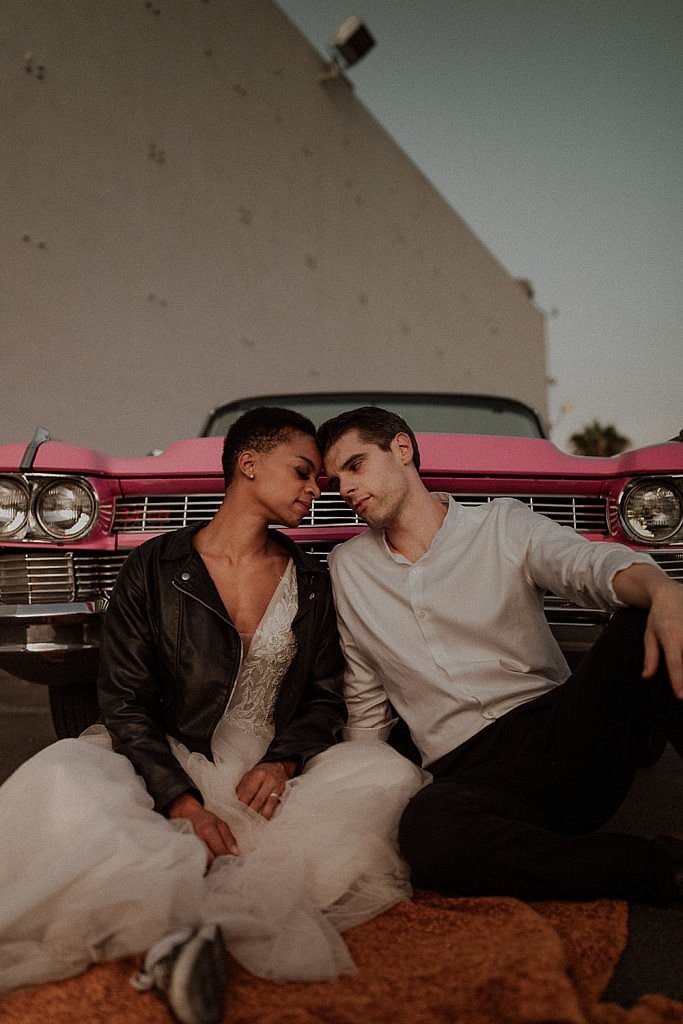Fun Las Vegas elopement with vintage pink caddy. Brides fluffy wedding dress and black leather jacket look amazing with her shaved head