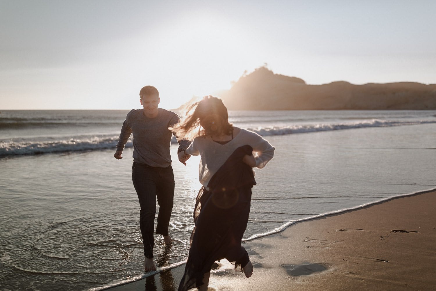 Bride and groom run along the beach at their Oregon coast elopement. The water at Cape Kiwanda in Pacific City was cool to touch but gorgeous to look at
