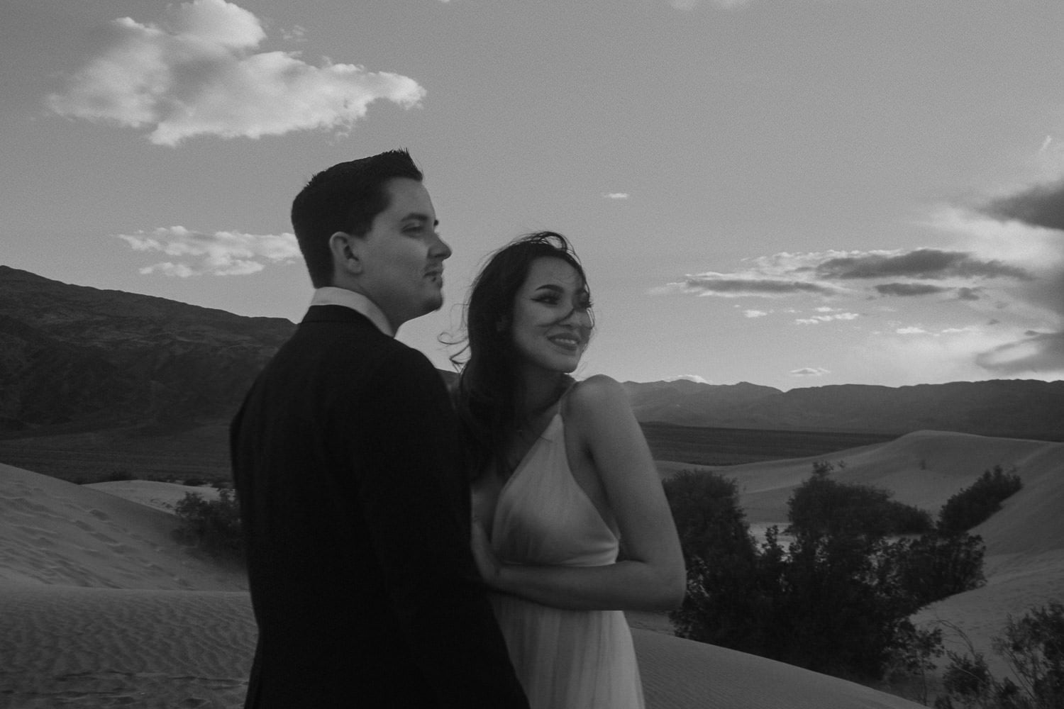 Black and white image of an Oregon elopement couple in the desert at sunset. The bride's hair blows in her face from the wind as they both look out into the distance at the amazing scenery they are about to get married in.