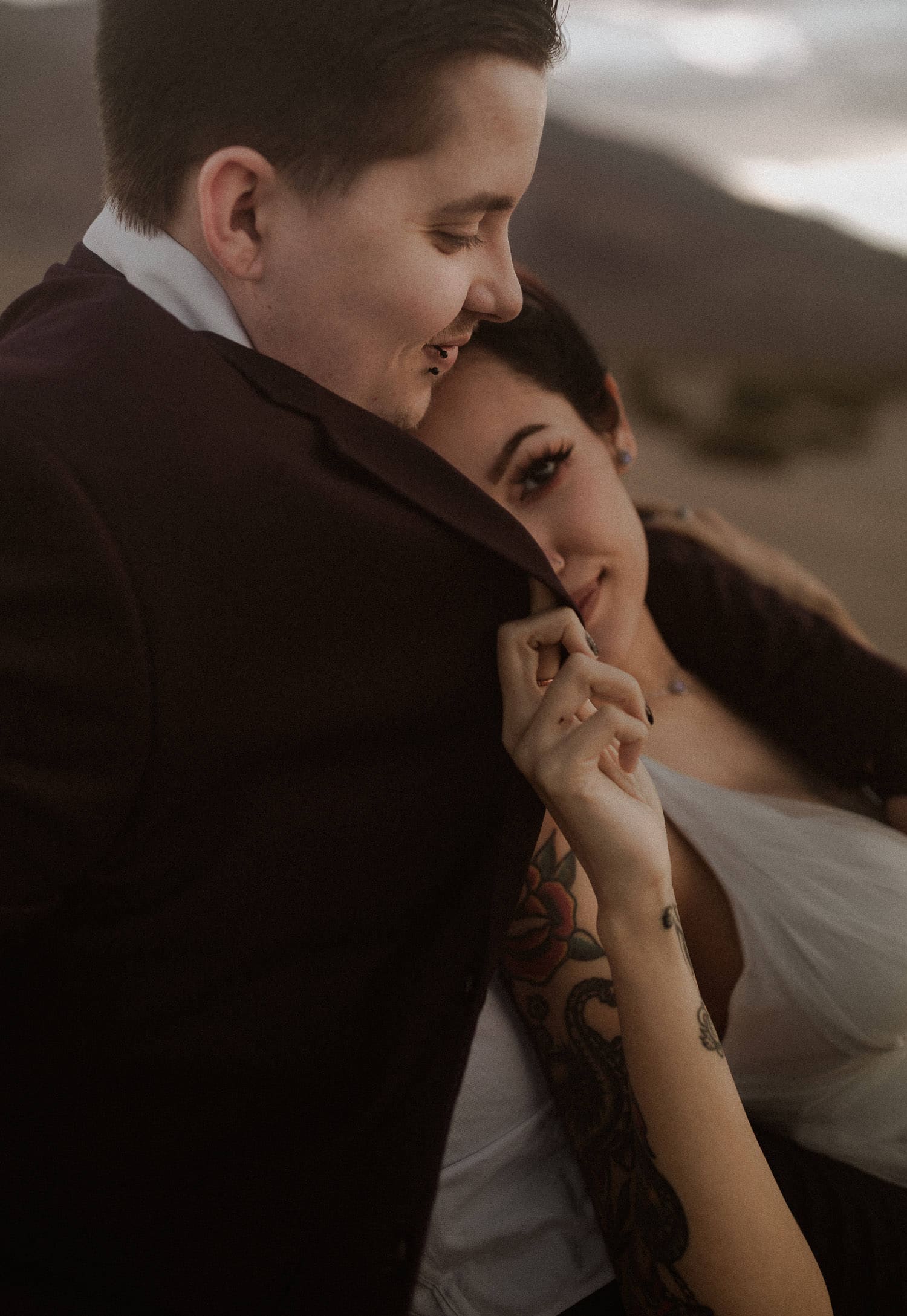 Cute elopement bride hides her face in her grooms jacket and smiles at the camera. Her groom looks down at her face and holds her close. Their intimate small wedding was perfect in the Oregon desert