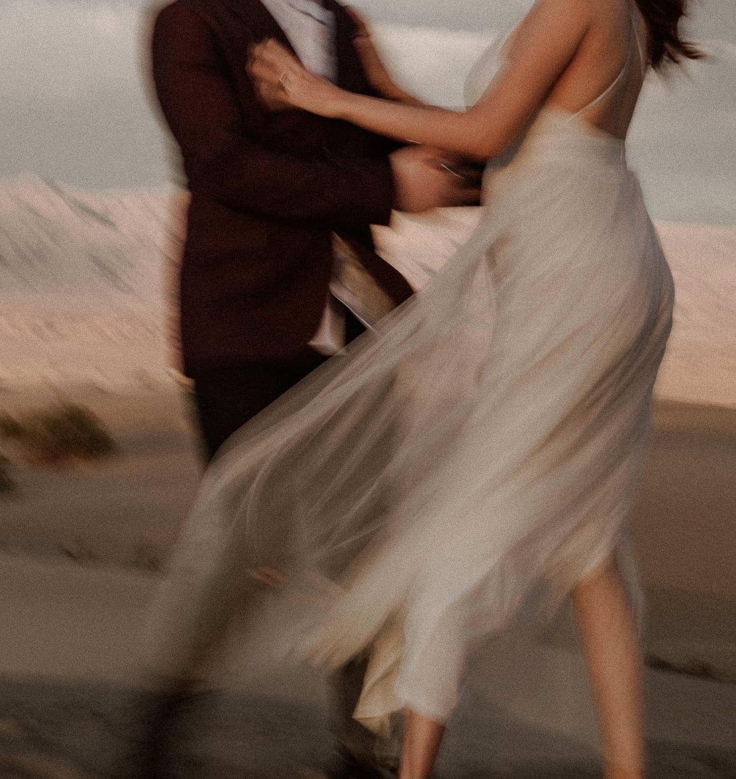 Elopement couples first dance in the sand dunes while the sun slowly sets behind the mountains. Brides dress blows in the wind