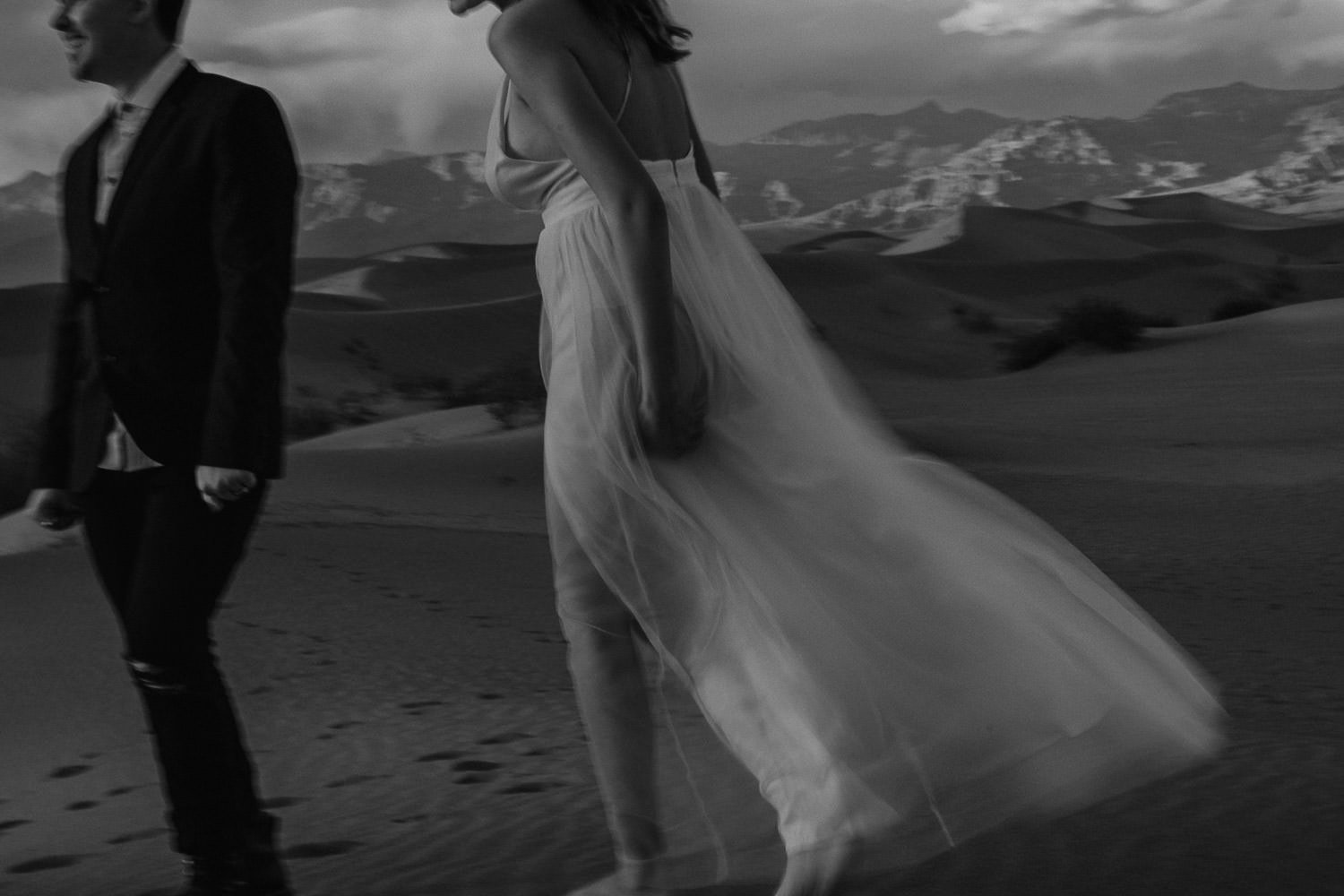 Black and white photo of bride's dress blowing in the desert wind