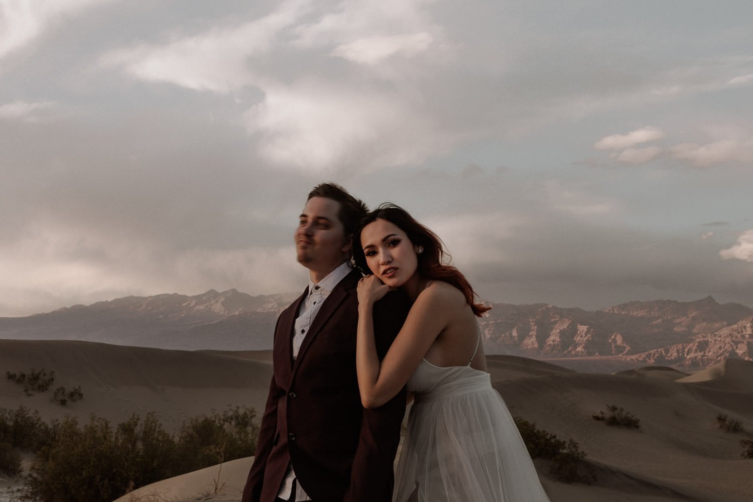 Elopement couple snuggle against the wind in the desert while the clouds move above them. This intimate elopement ceremony in Oregon had amazing views of sand dunes and mountains.