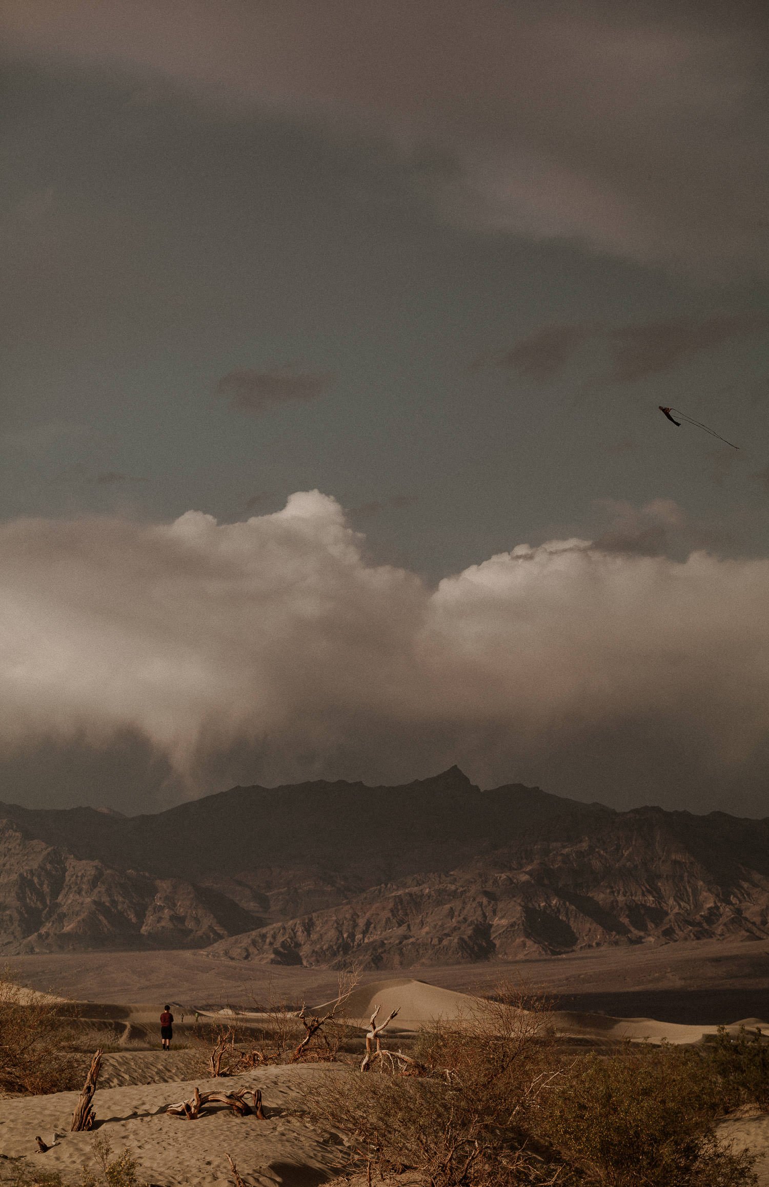 Sand Dunes landscape photo surrounded by mountains and clouds in the evening light. Lone man flies a red kite in the distance