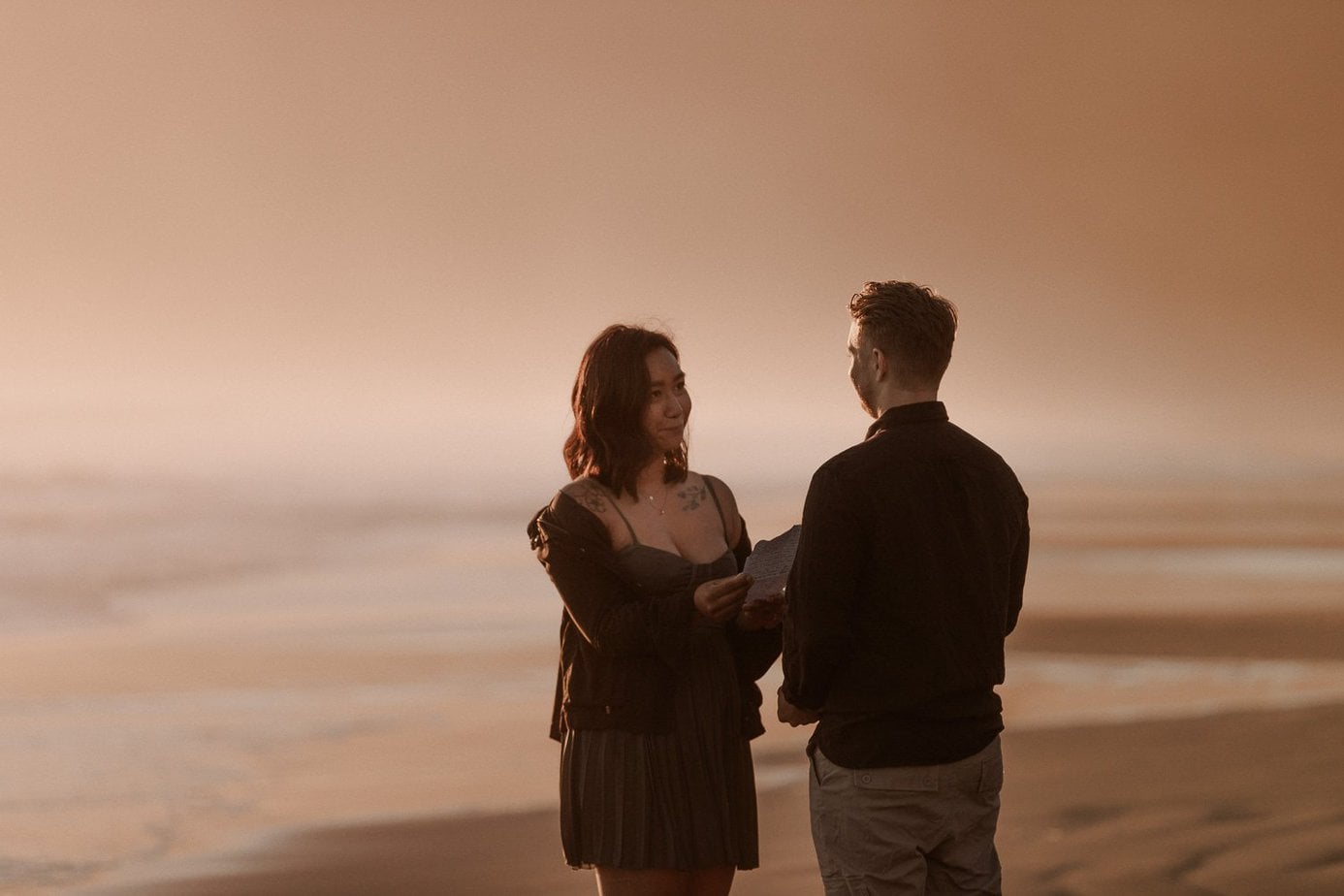Sunset Oregon coast elopement where the ocean mist glows in the sunlight. Couple reads their handwritten vows to each other