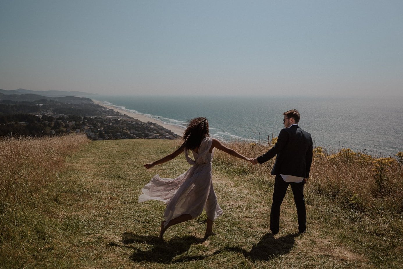 Bride and groom dance on the hillside before their God's Thumb elopement. They loved the adventure of their elopement day on the Oregon coast. Her lavender wedding dress blows in the wind like a fairytale