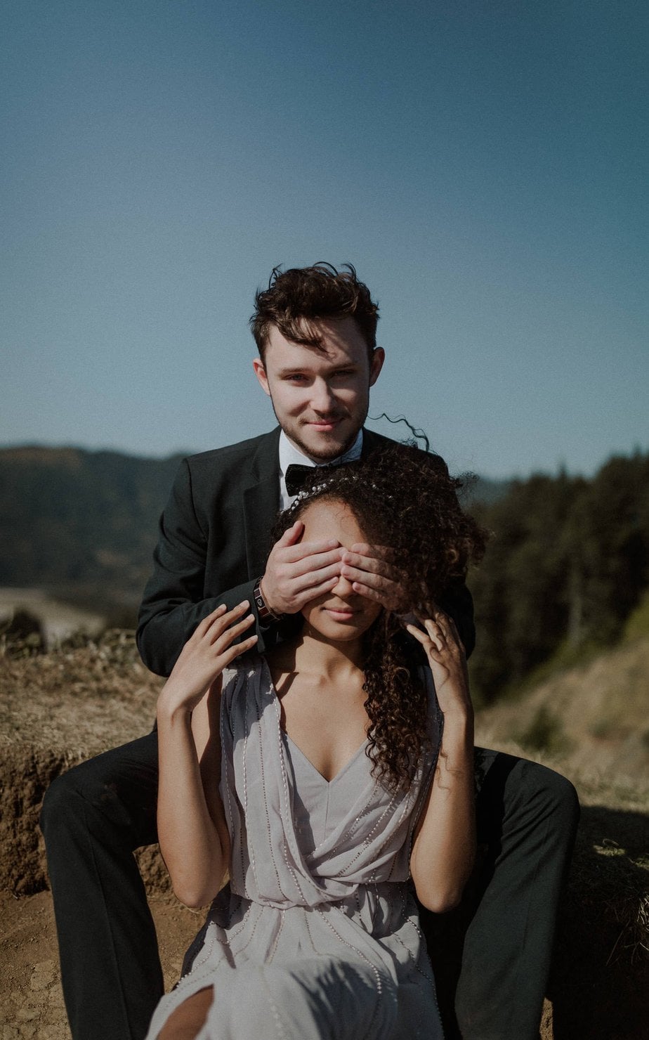 Groom covers brides eyes as the wind whips her hair around during their adventure elopement