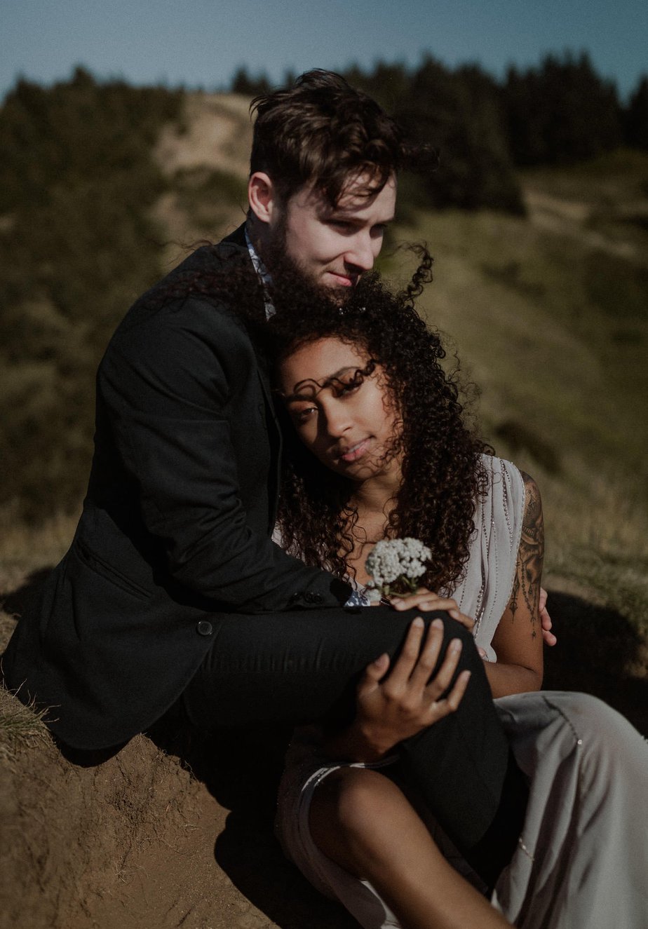 Bride leans into her groom as he warms her from the coastal winds. Her hair blows in her face. This God's thumb elopement was so wonderful and intimate with just the couple and their Oregon elopement photographer