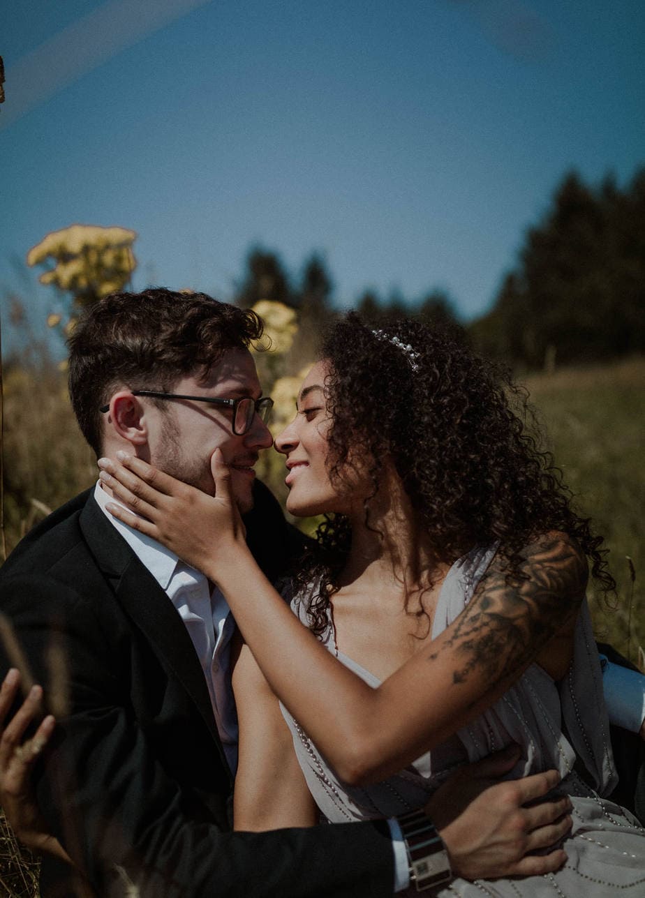 Beautiful bride snuggles against her partner. The sun is bright on their faces and makes the yellow wildflowers stand out against the blue skies