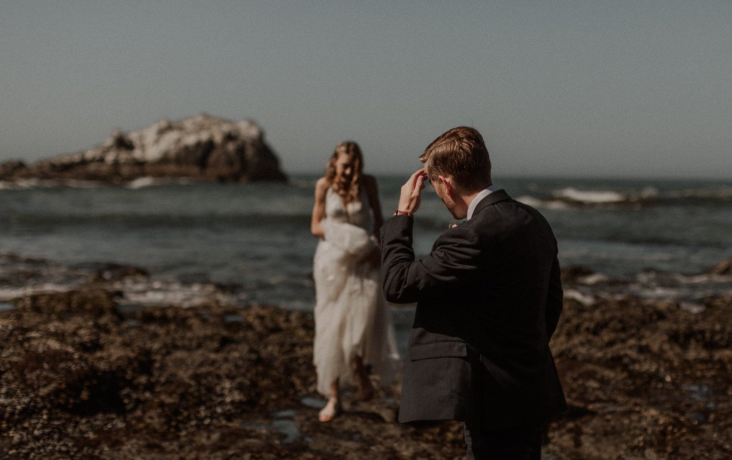 Oregon coast elopement at the Yaquina Head lighthouse on Cobble Beach. Groom gets emotional looking at his bride walk towards him. Eloping on the Oregon coast gives you the best of both worlds with the beach and amazing views.
