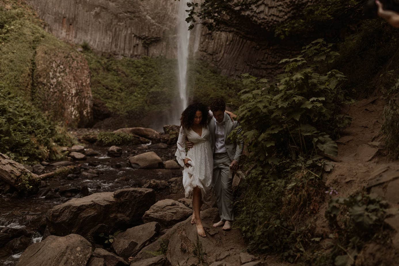 Bride and groom hike over the rocks at Latourell Falls
