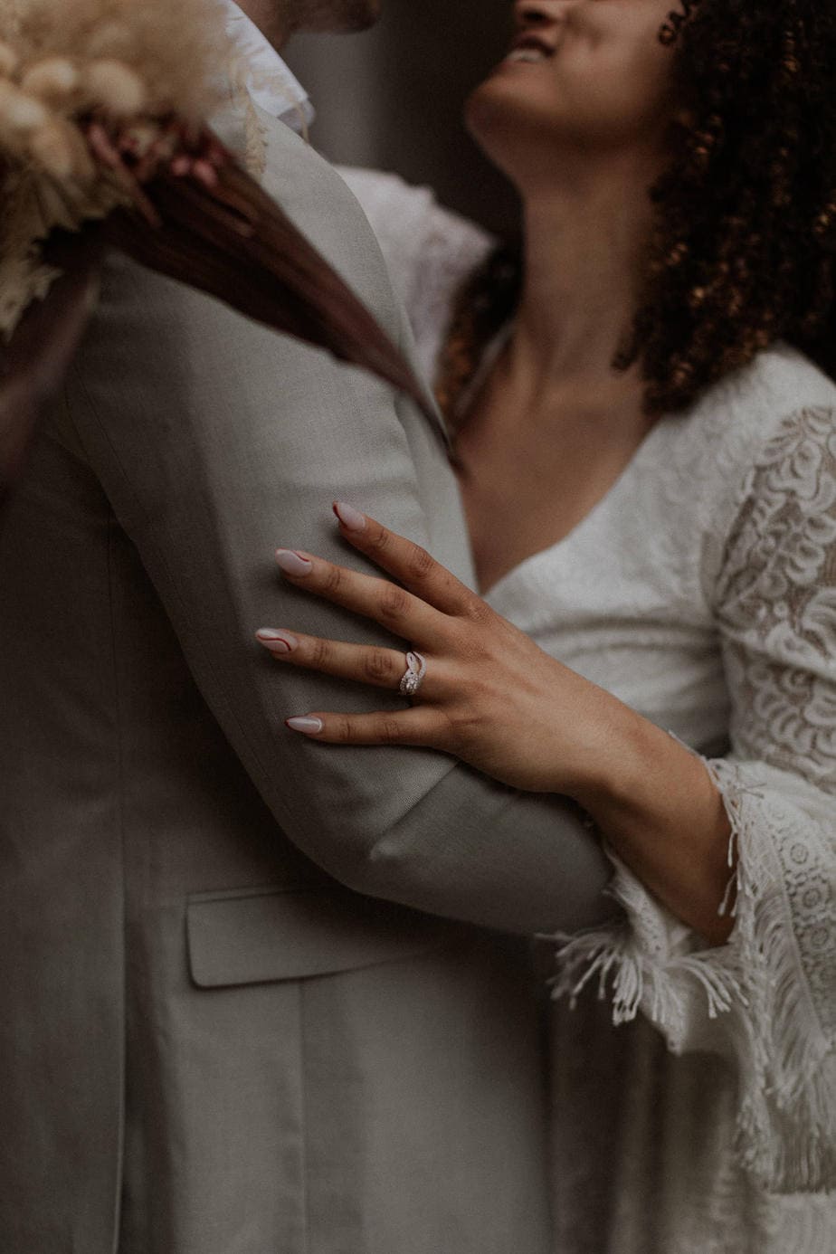 Close up image of brides ring and her boho dress with fringe sleeves