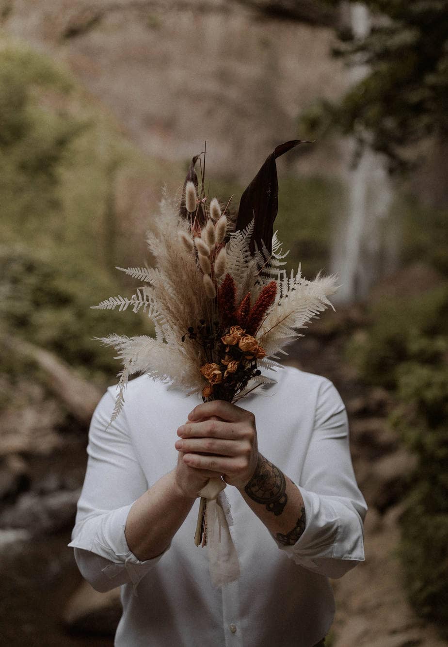 Groom at Latourell Falls elopement holds the dried bouquet in front of his face. Edgy bridal photos