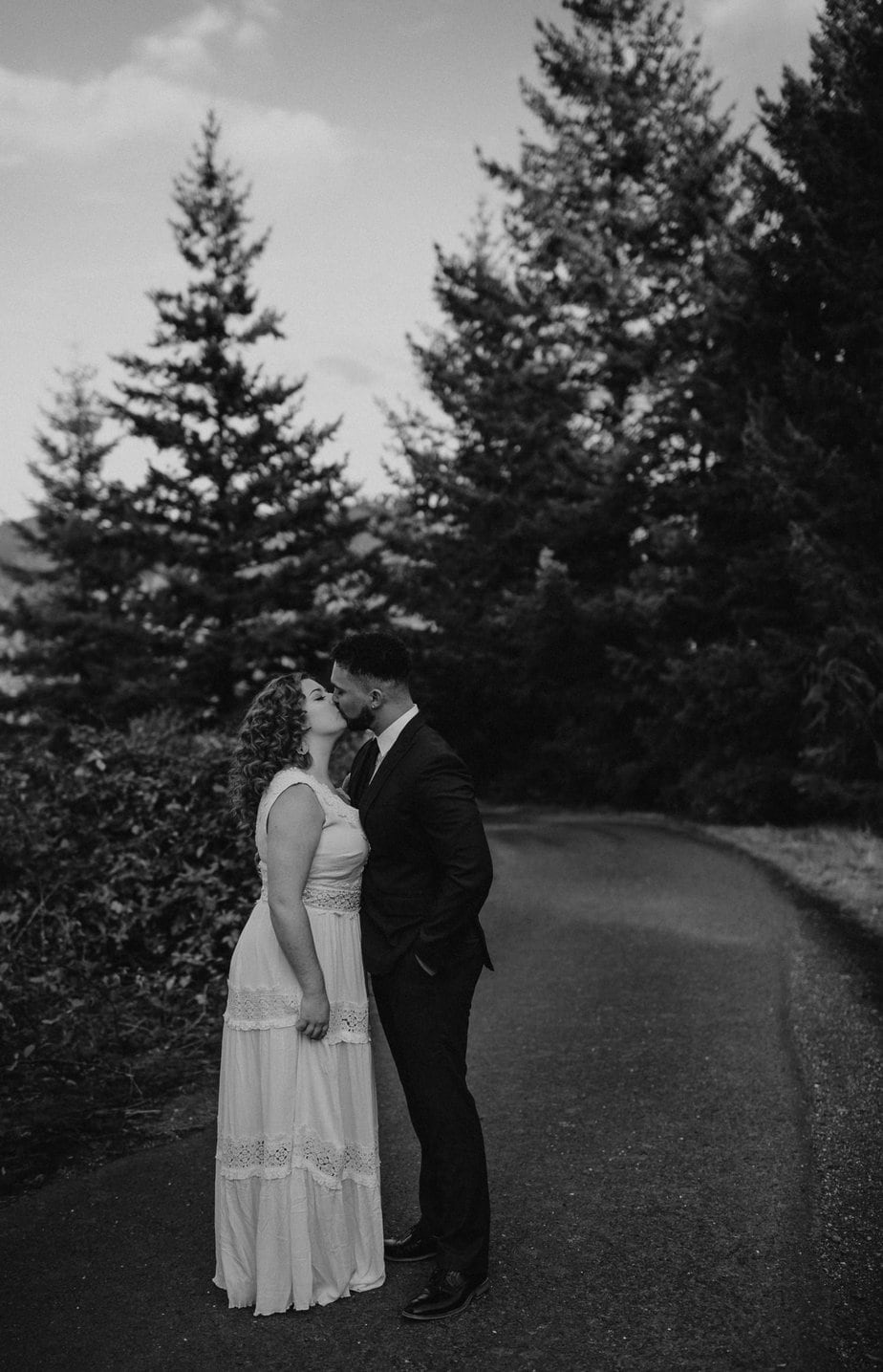 Black and white image of wedding couple kissing at Government Cove. Couple stands in pathway and the trees surround them.
