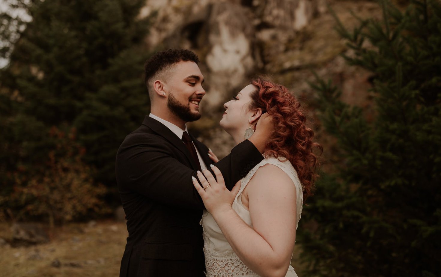 Bride and groom embrace at Government cove in the Columbia River gorge for their Oregon adventure elopement. Groom runs his fingers through the bride's bright red hair. The bride looks lovingly at her new groom