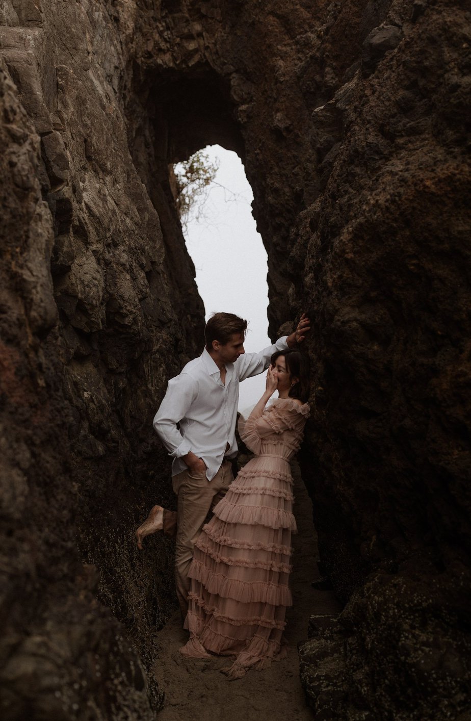Bride is bashful at her elopement ceremony on Neskowin Beach. Groom leans over her to kiss her in the cove in the rocks