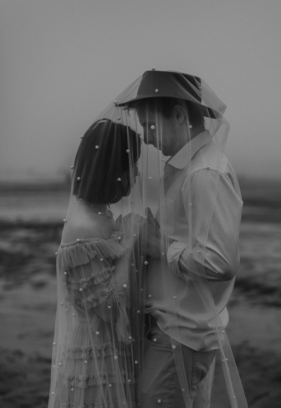 Wedding couple hold hands under veil at Neskowin Beach. This Oregon coast elopement was perfectly moody with all of the fog in the early morning.