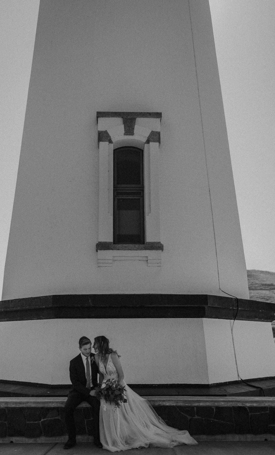 Bride and groom sit at the bottom of the lighthouse for their elopement on the oregon coast