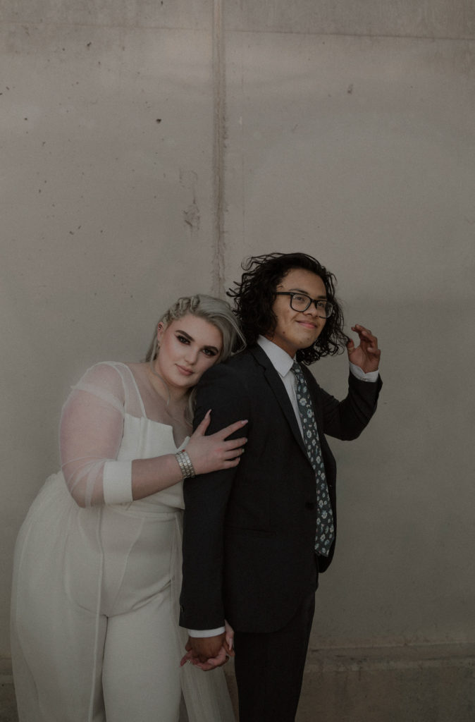 Wedding couple poses in front of concrete wall 