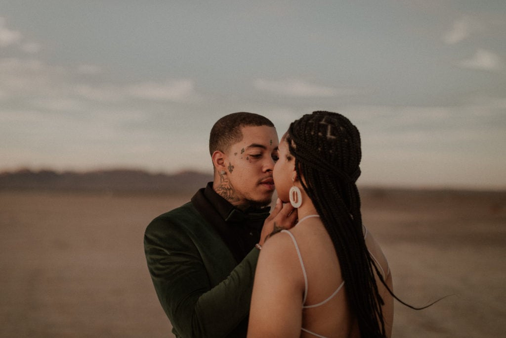 Newly eloped couple stand in dry lake bed. Groom holds his bride's face and pulls her in for a kiss