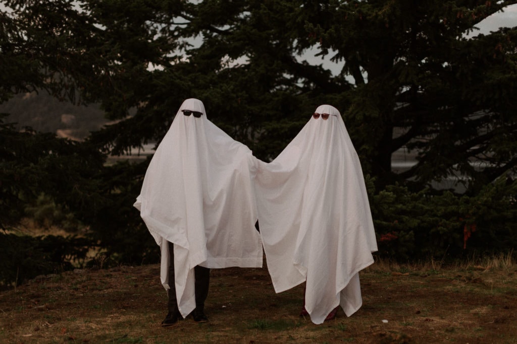 Funny ghost couples session in Oregon. couple in white sheets and sunglasses look at camera