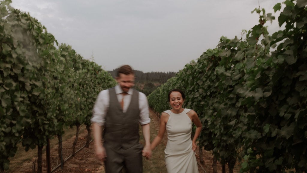 Wedding couple runs through a vineyard after their elopement ceremony while laughing. 