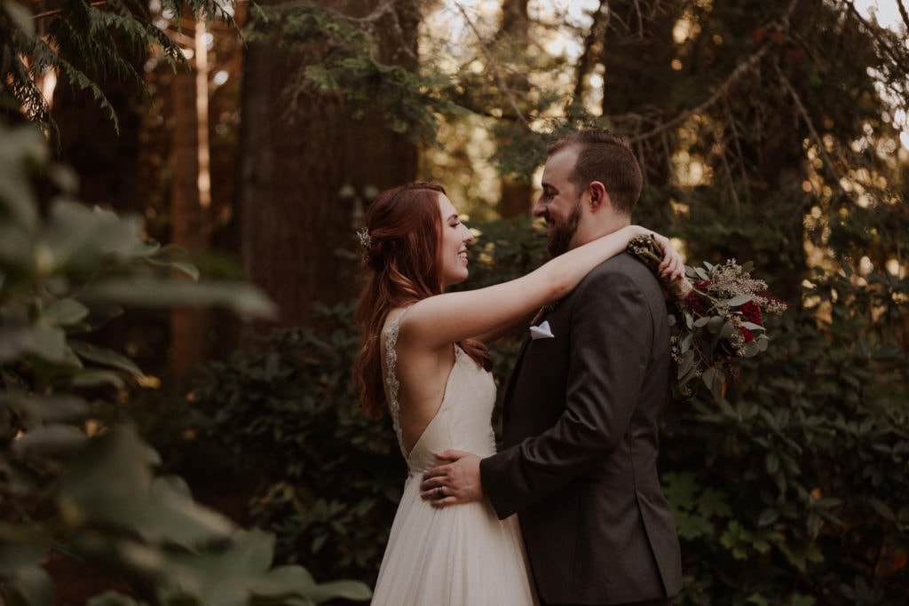 Bride and groom look into each others eyes in the middle of the Oregon forest. Bride has red hair and has her arms around grooms neck