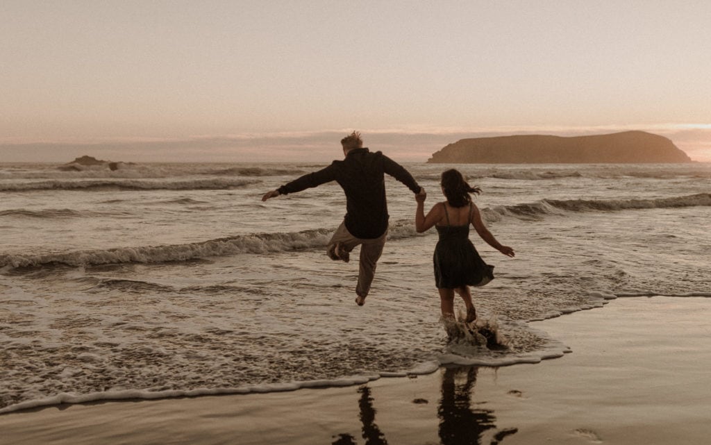 Engaged couple run into the cold ocean on the Oregon Coast at sunset