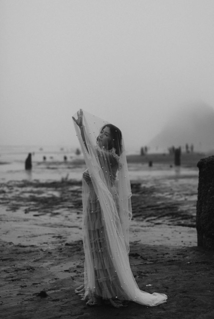 Bride stands on Neskowin beach in a cathedral veil
