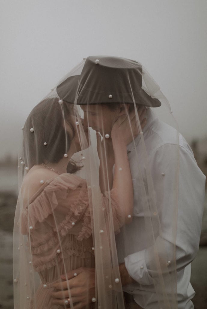 Bride and groom kiss under her veil that is covered in pearls