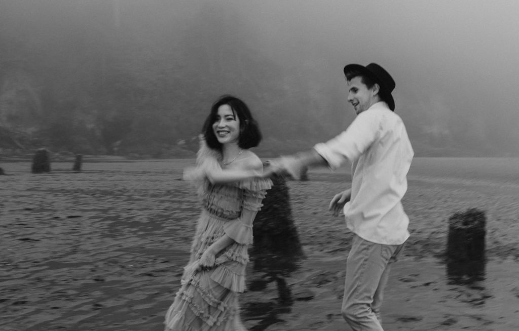Black and white image of eloping couple dancing in the sand and laughing