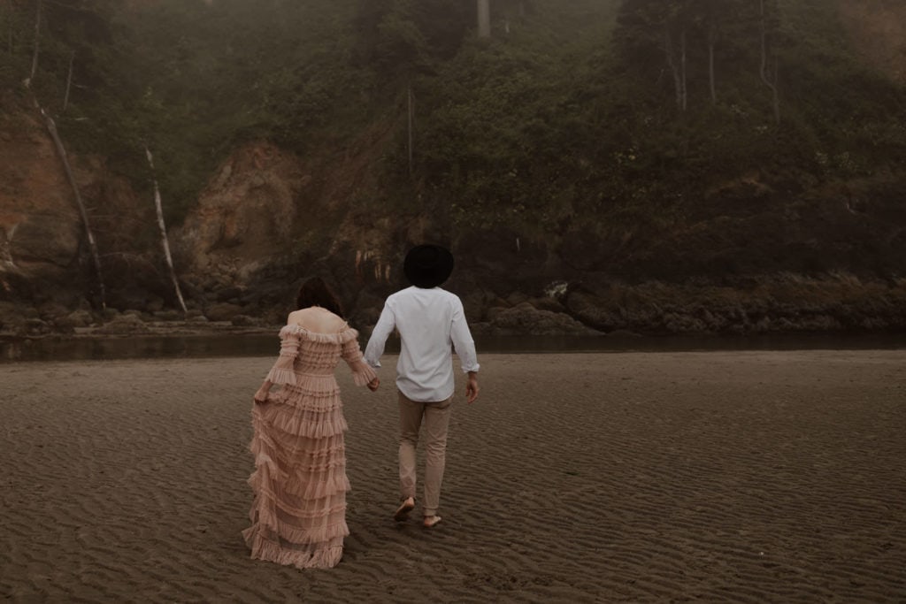Eloping couple walks towards proposal rock in Neskowin, Oregon for their elopement