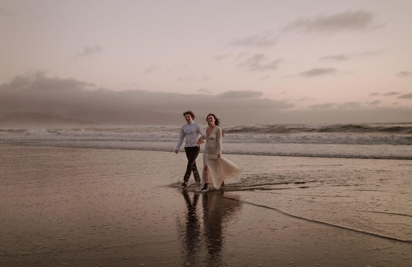 Bride and groom walk along Oregon coast after their adventure elopement. The water has smoothed the sand