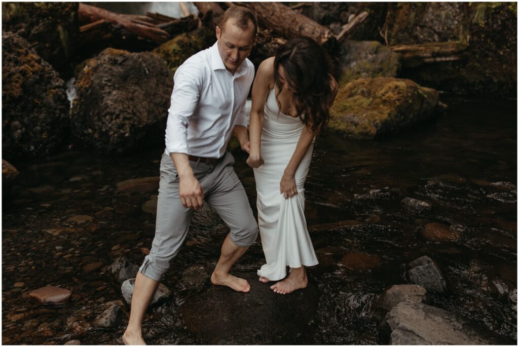 Groom helps bride navigate the cold waters of Wahclella falls while barefoot